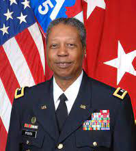 Adolph McQueen in uniform with flag in background.